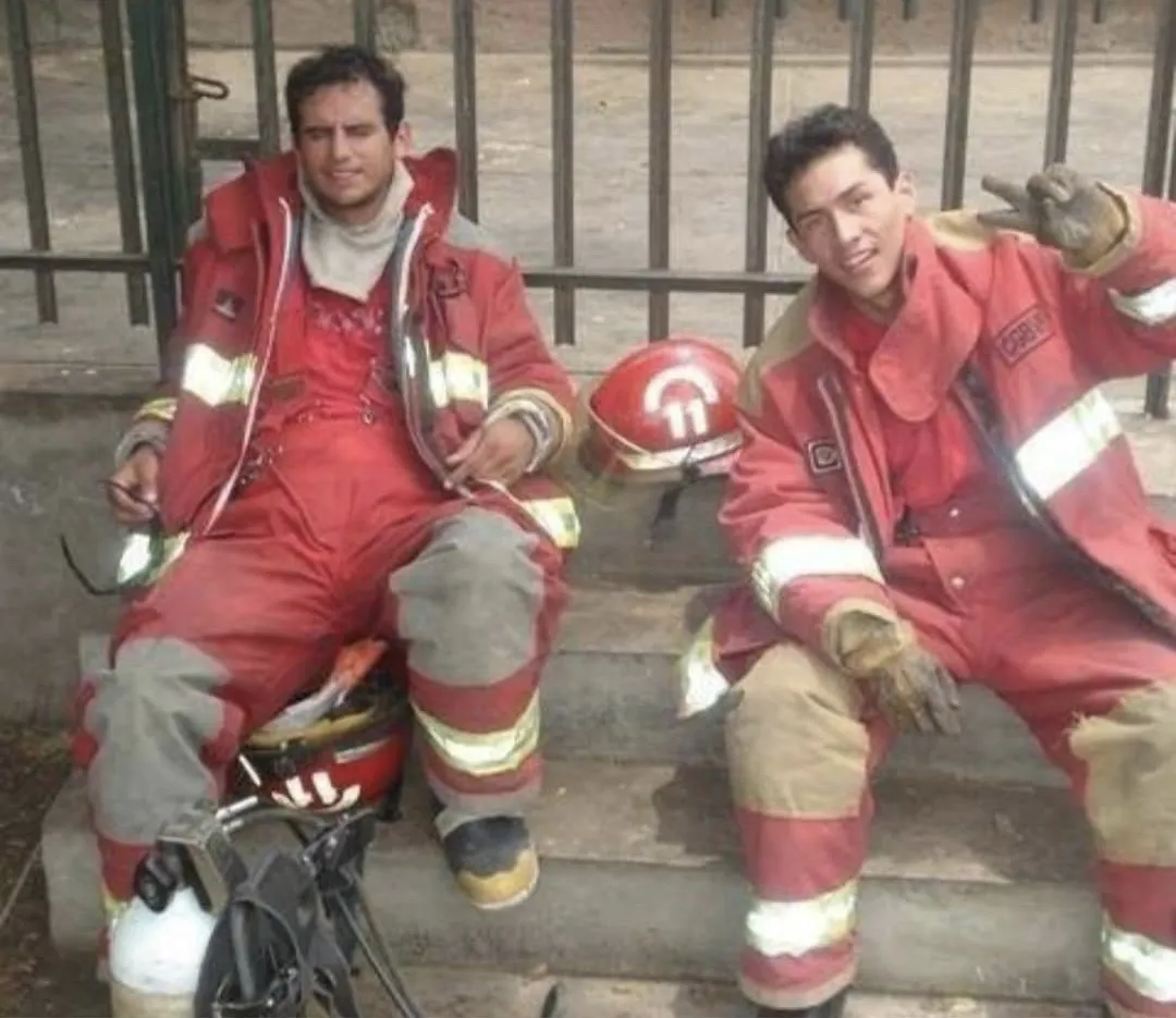 Josué Moya de la Cruz con su uniforme de bombero voluntario, junto a un compañero